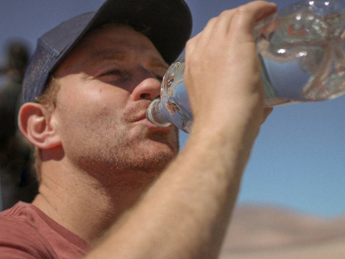 Man met pet die water drinkt uit een fles (illustratiefoto)